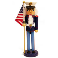 nutcracker of Marine in dress blues stands at attention holding an American flag, parade cap with USMC emblem, faux fur beard